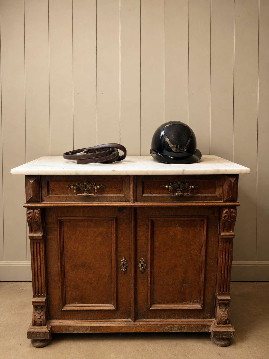Black riding helmet and coiled bridle resting on a marble sideboard against pale wood paneling.